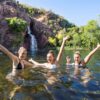 Three women waving in a waterfall plunge pool in Litchfield National Park