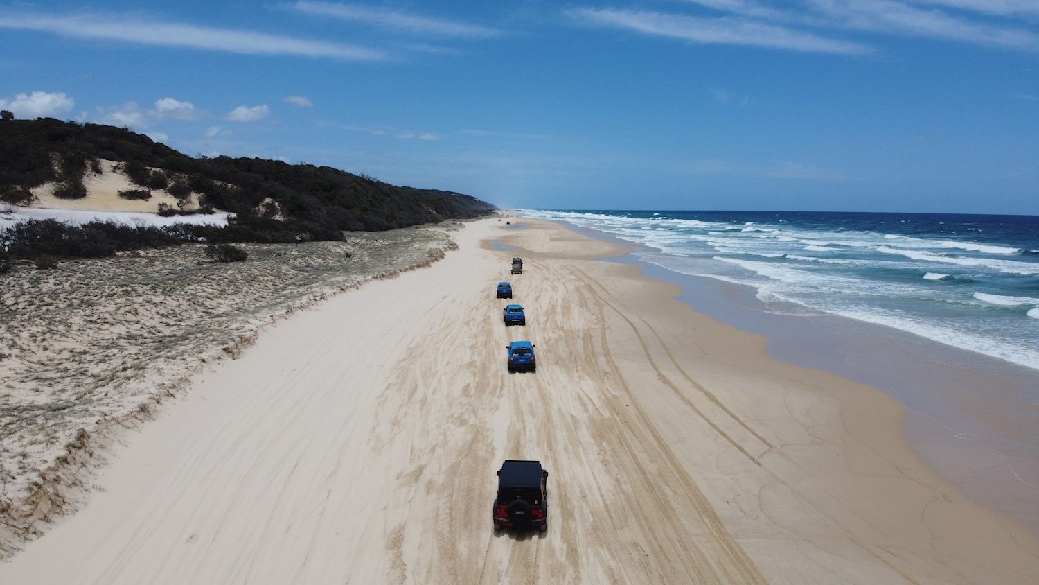 Convoy of 4WDs driving along a wide sandy beach