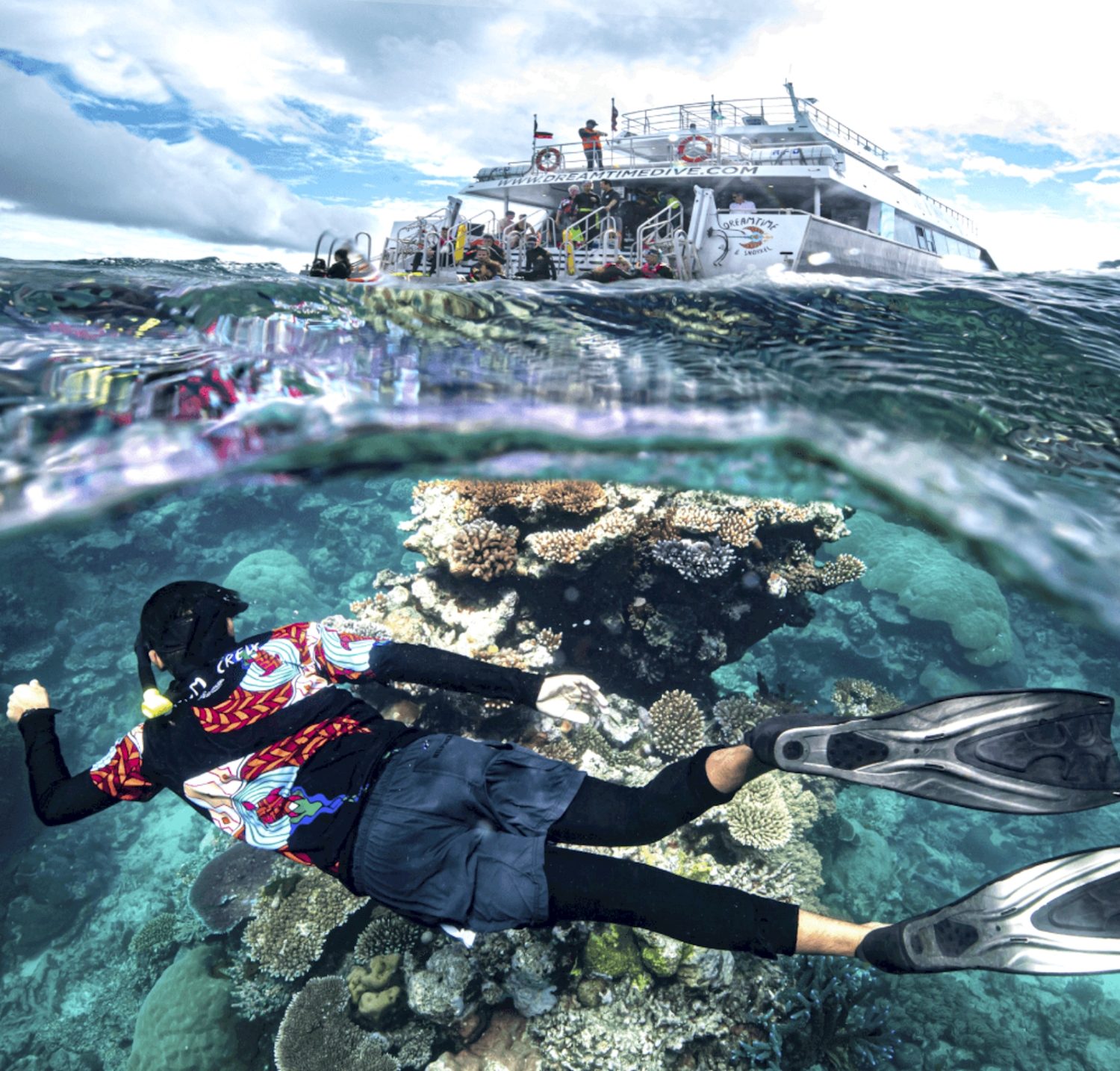 Snorkeller gliding over coral with the reef boat behind