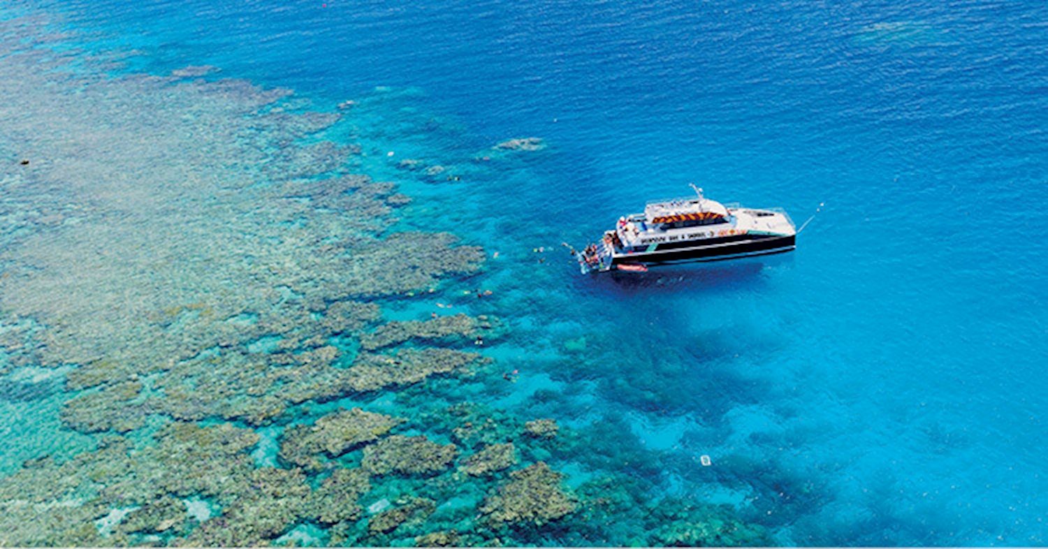 Reef boat moored beside coral reef in turquoise water, seen from above