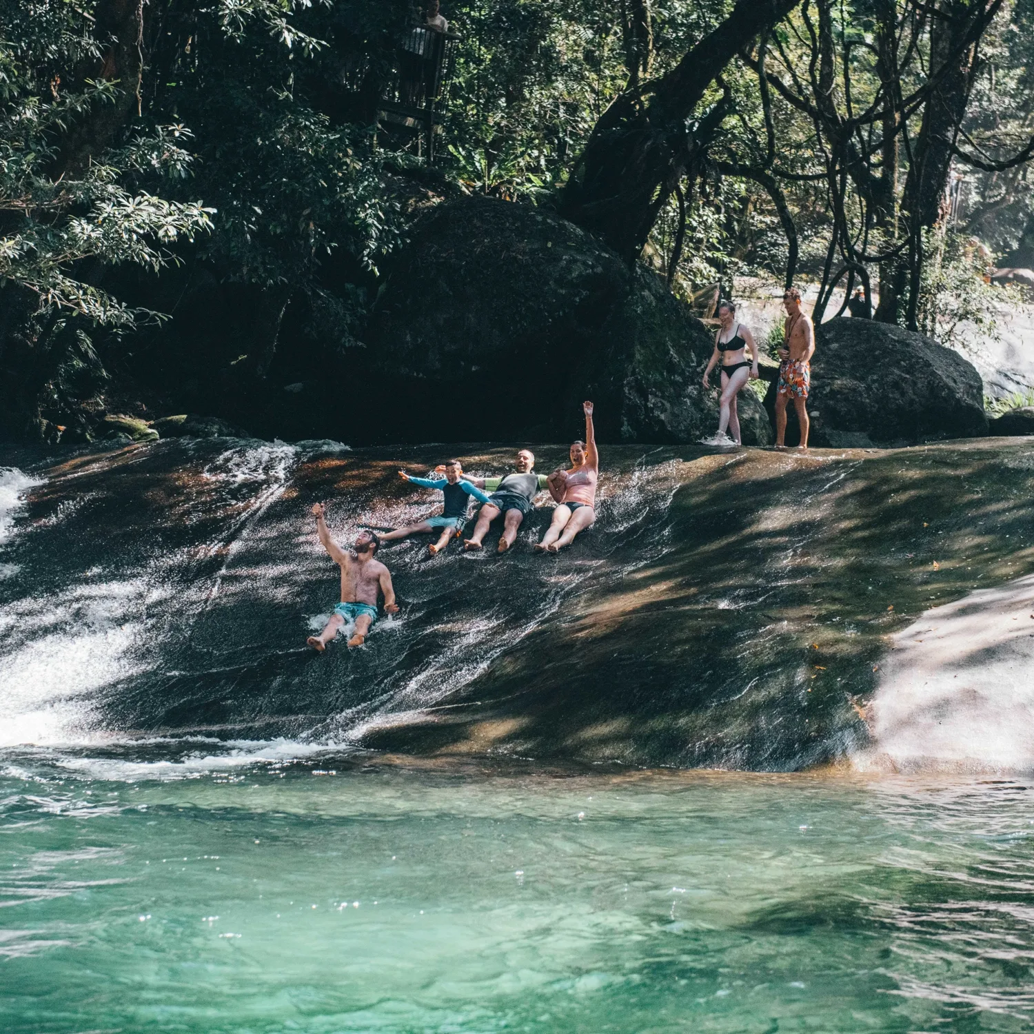 Travellers sitting on rocks at a rainforest waterfall in the Atherton Tablelands
