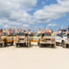 Travellers waving from a convoy of 4WD vehicles on a K’gari beach