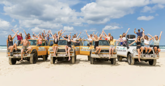Travellers waving from a convoy of 4WD vehicles on a K’gari beach