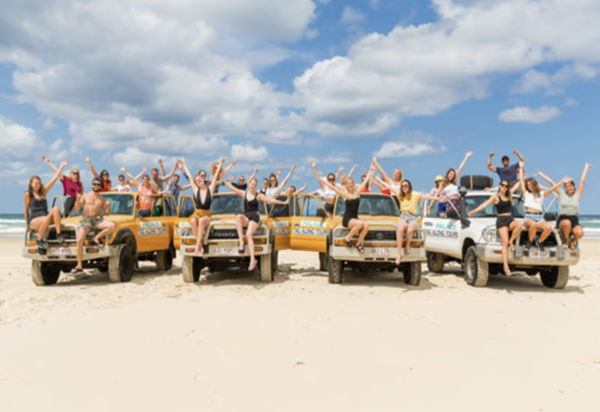 Travellers waving from a convoy of 4WD vehicles on a K’gari beach