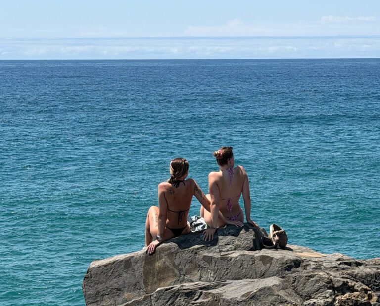 Two travellers sitting on coastal rocks above the ocean at Noosa