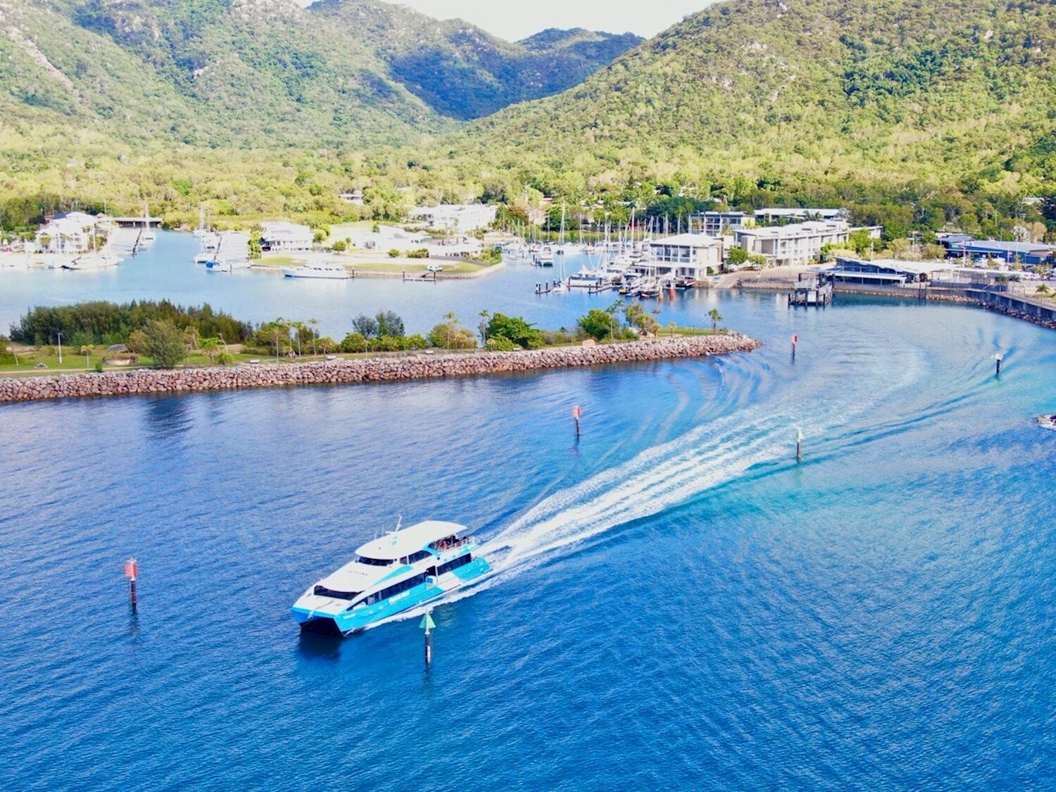 SeaLink catamaran crossing calm blue water towards a marina below green hills